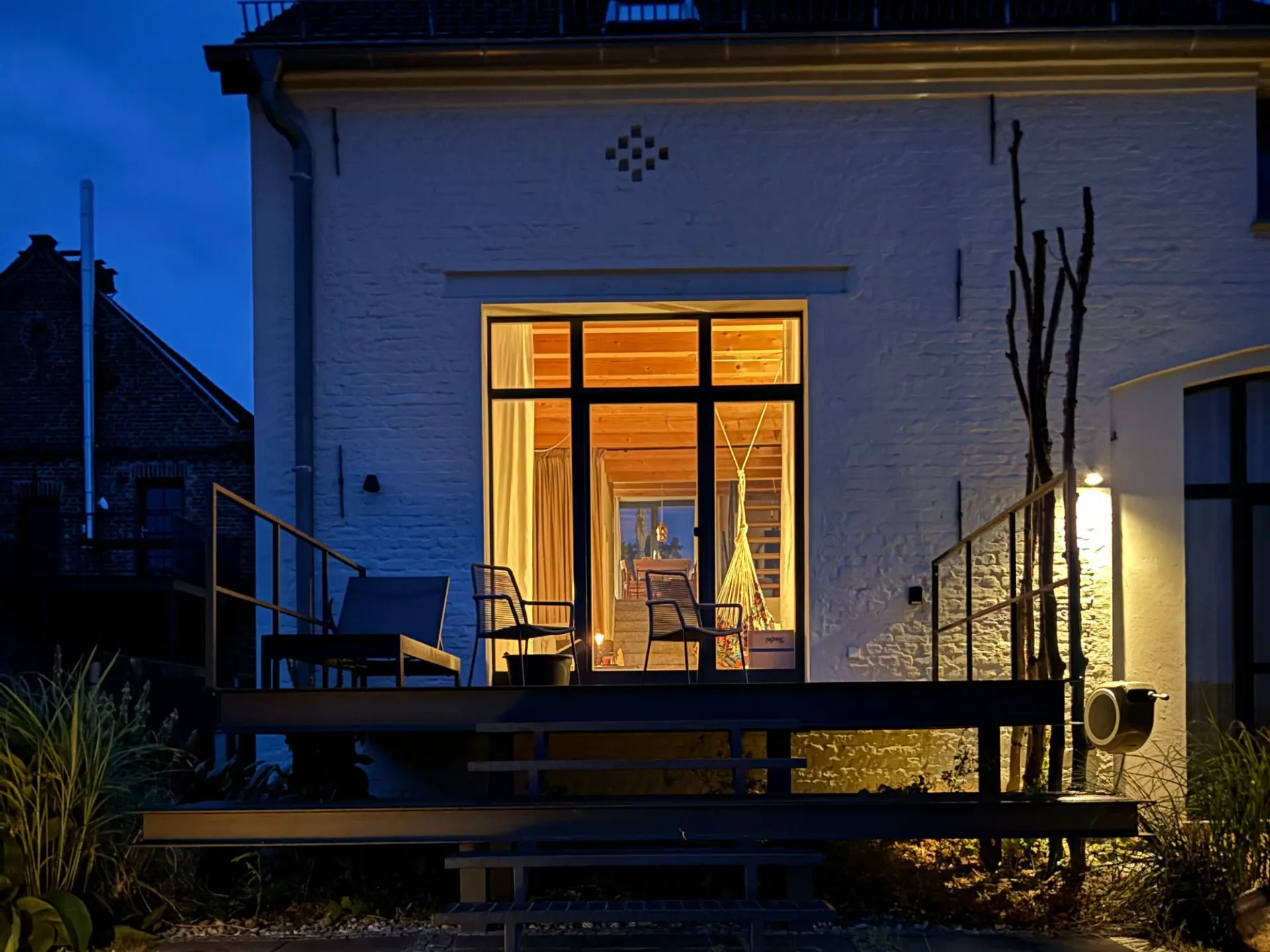 Haus bei blauer Stunde: beleuchtete Metallterrasse und warm erleuchtete Fensterfront