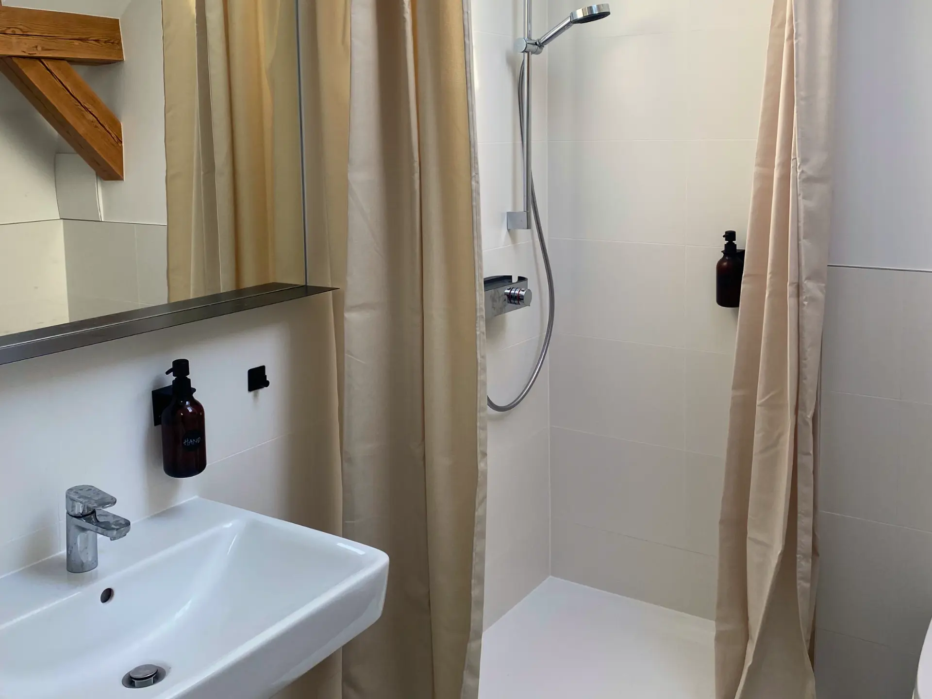 Helles Duschbad mit offener Dusche, weißem Waschbecken und sichtbarem Holzbalken