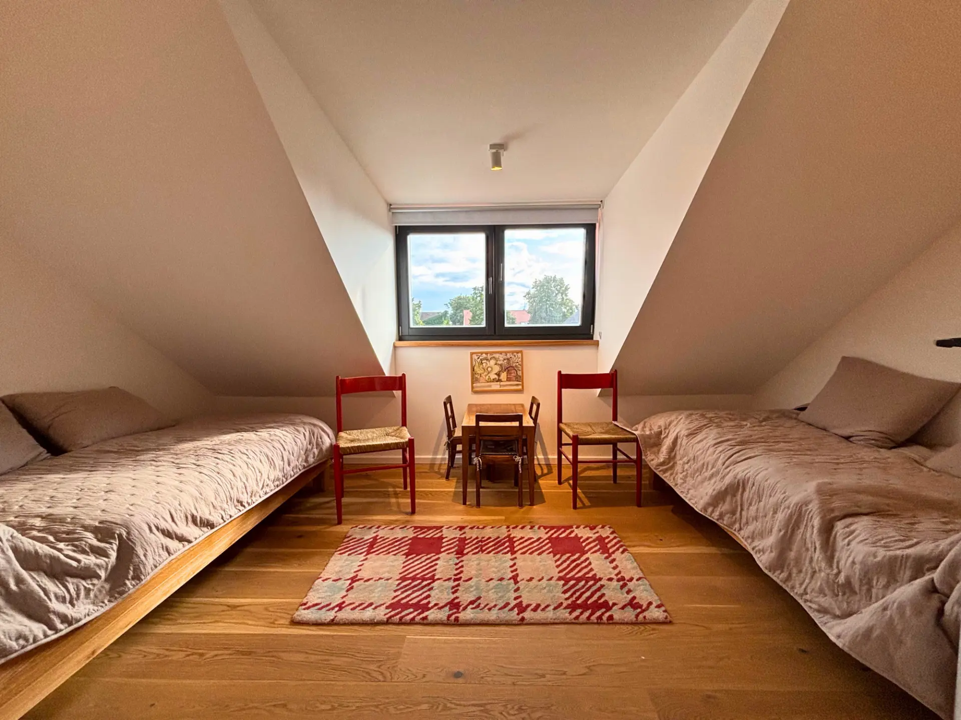 Zimmer mit zwei Einzelbetten, roten Holzstühlen und kleiner Kindersitzgruppe am Fenster
