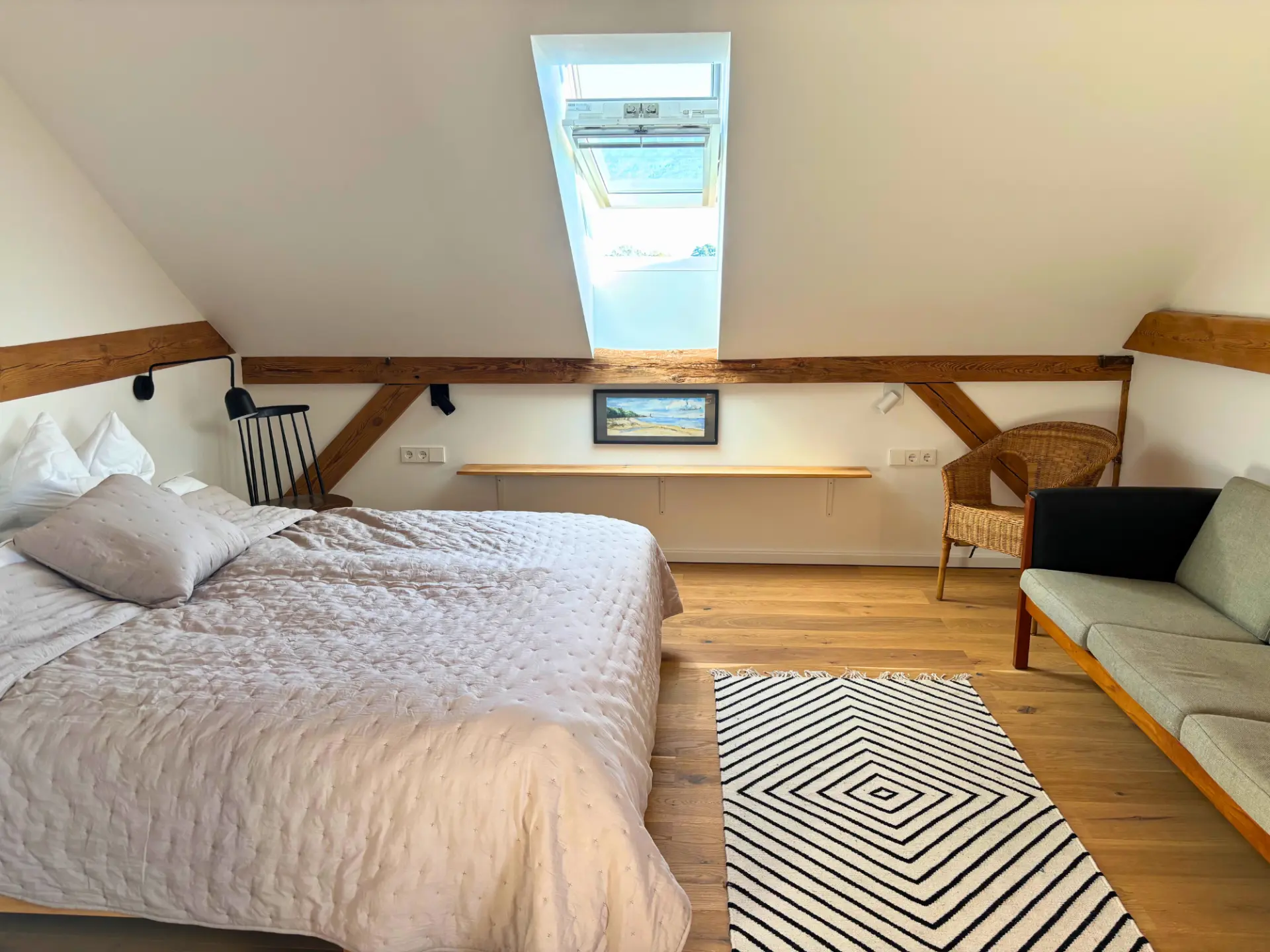 Schlafzimmer unterm Dach mit Doppelbett, Rattansessel und weiß gemustertem Teppich