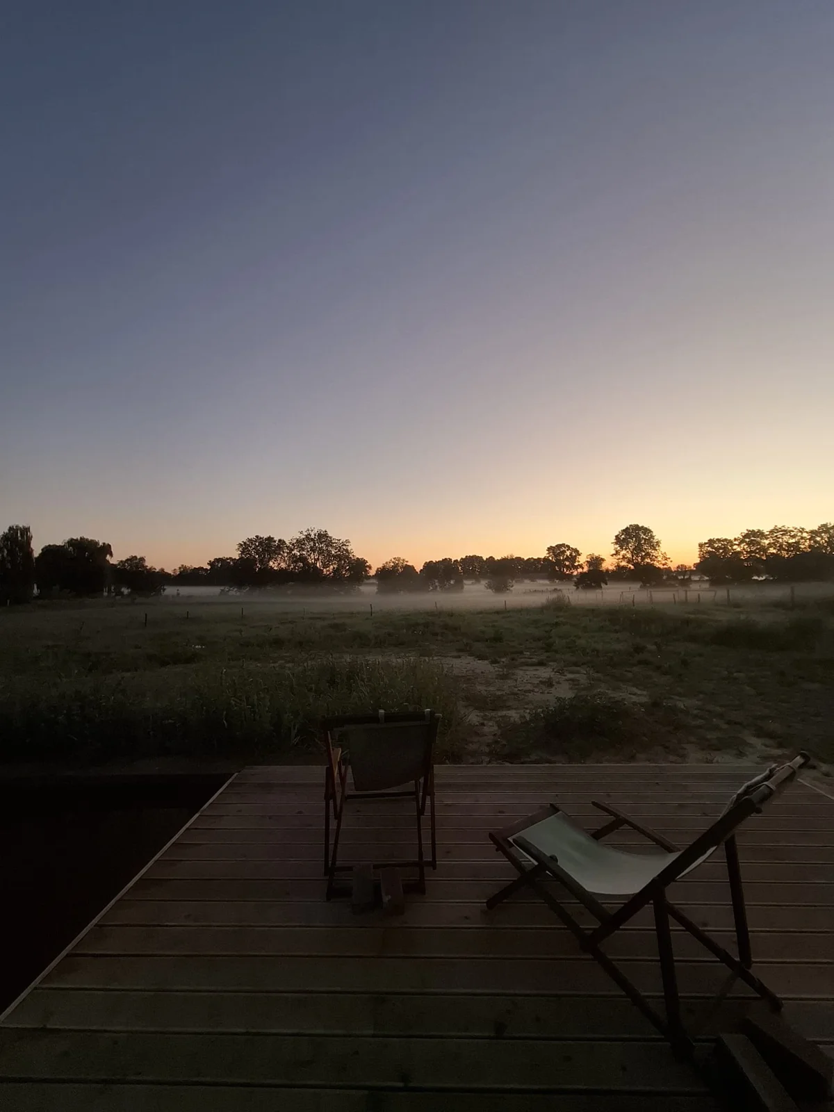 Morning mist over the meadows at sunrise, two deck chairs on the wooden terrace