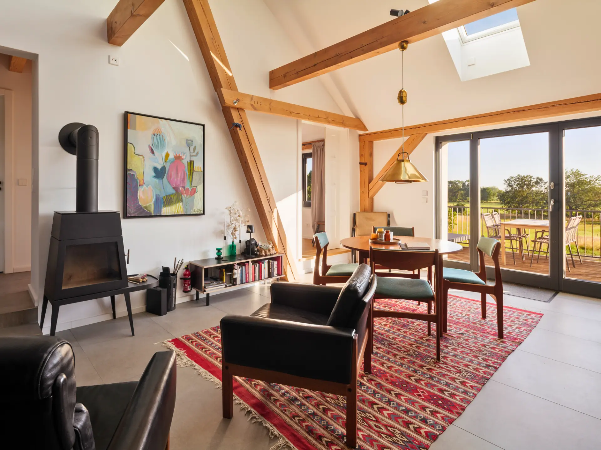 Wohn- und Essbereich mit Kamin und Blick durch die Fensterfront auf die Holzterrasse und die Wiesen