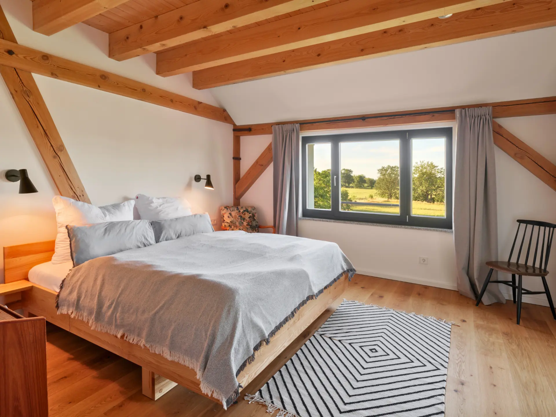 Schlafzimmer mit Doppelbett unter den Sichtbalken und weitem Ausblick in die Wiesenlandschaft