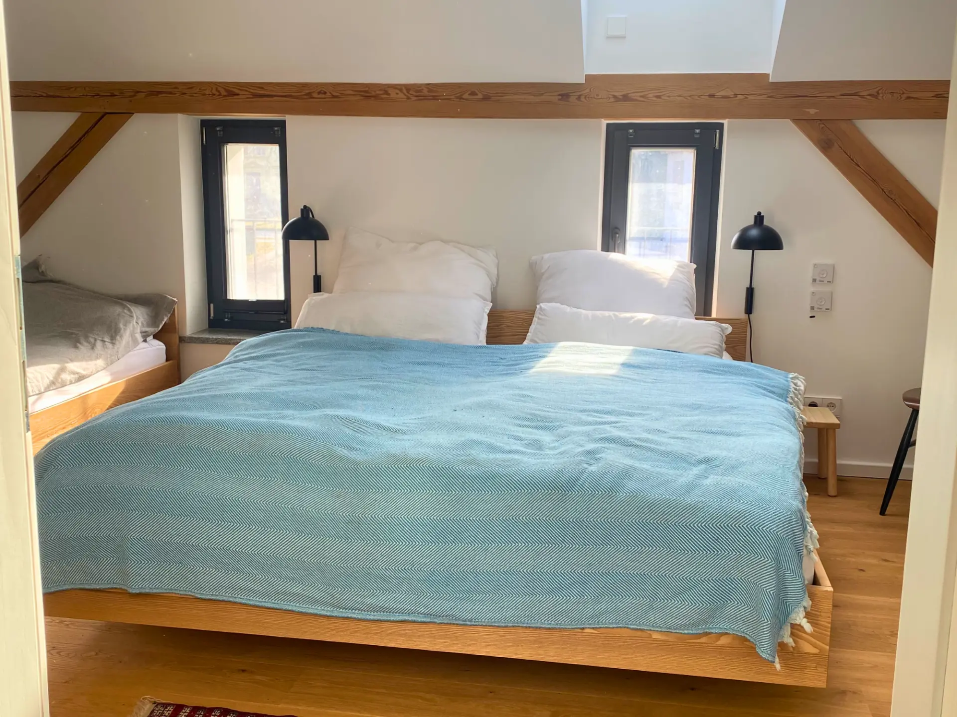 Familienschlafzimmer mit Doppelbett in hellblauer Tagesdecke und Einzelbett in der Nische unter den Holzbalken der Dachschräge