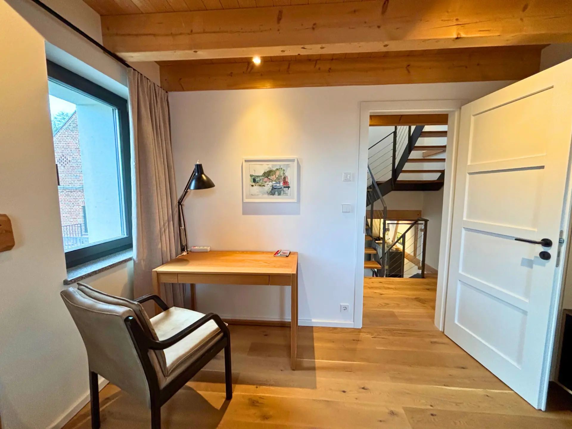 Schreibtisch mit Arbeitsleuchte und Sessel, Blick zum Treppenhaus