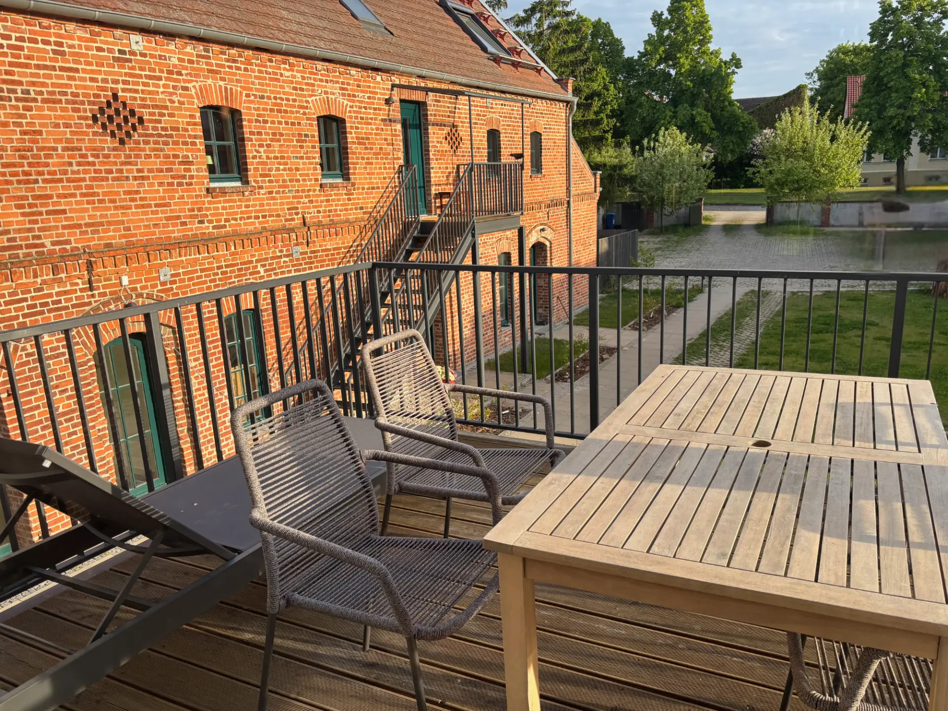 Balkon mit Esstisch, Geflechtsesseln und Liegestuhl, Blick über den Hof