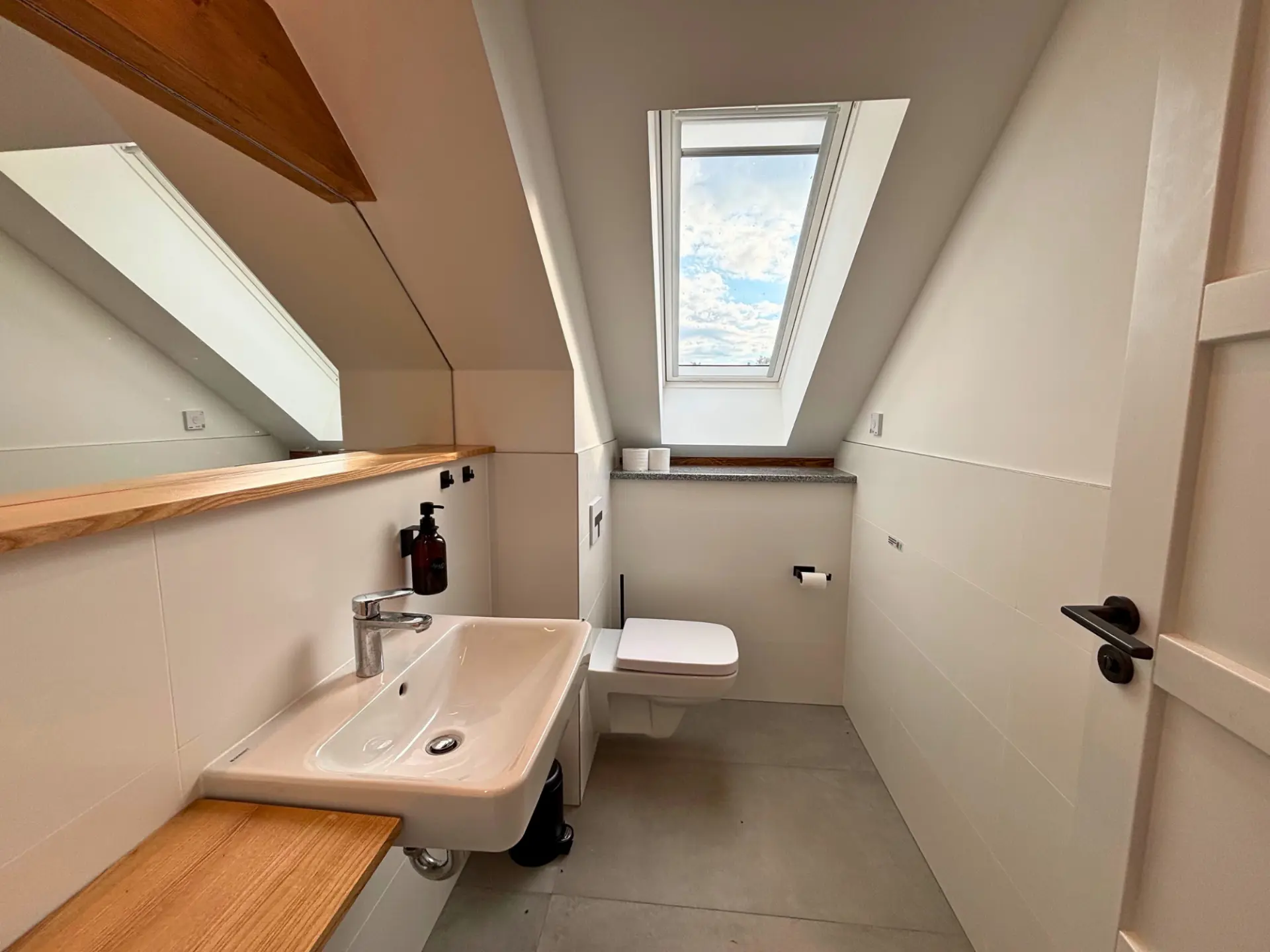 Tageslichtbad unterm Dach mit weißem Waschtisch, WC und Dachfenster in den Himmel