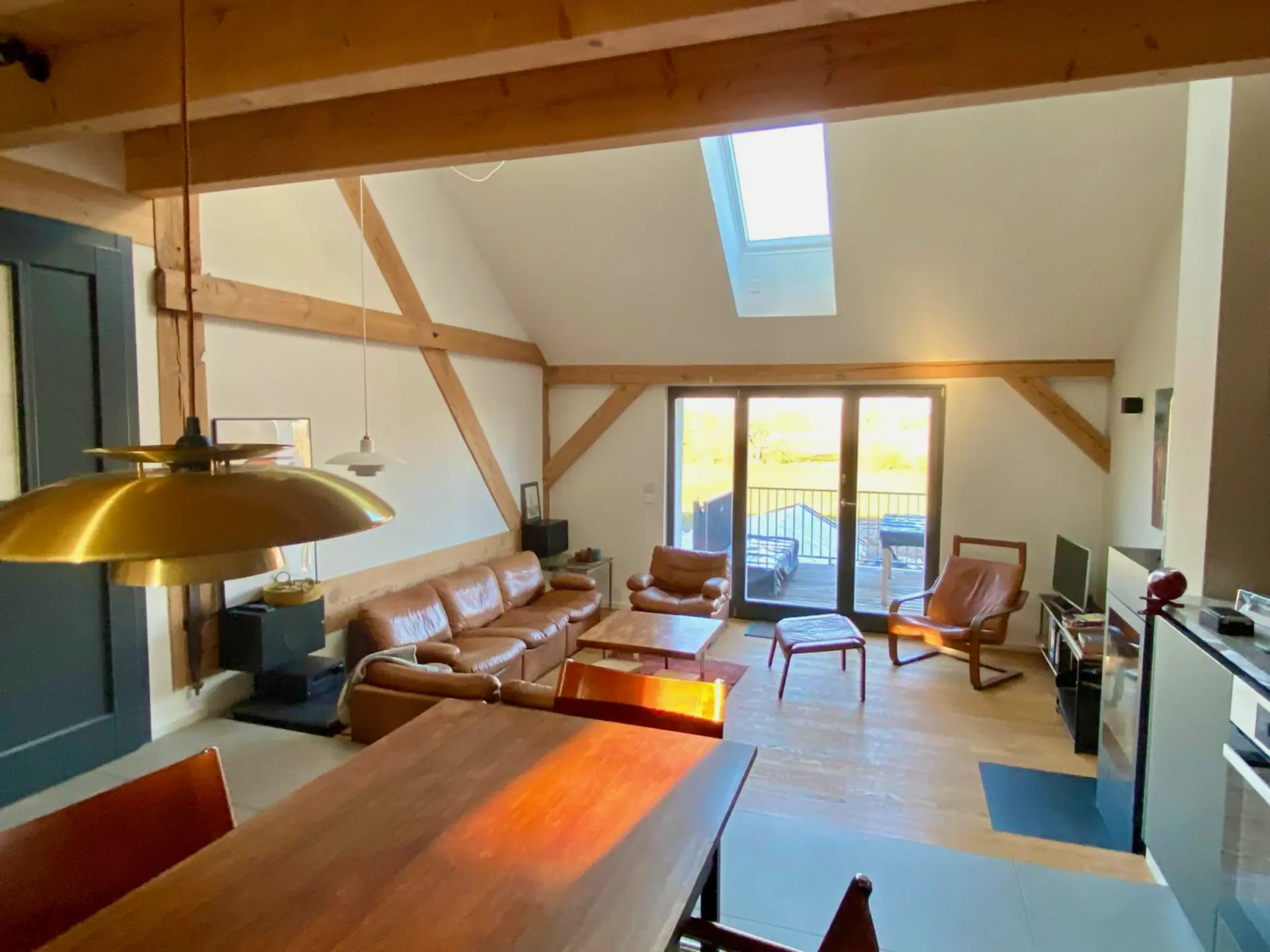 Ess- und Wohnbereich mit langem Holztisch unter Messing-Pendelleuchte und Blick in die Landschaft